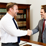 **An auctioneer shaking hands with a consignor in a well-lit office, both smiling, with valuable antiques displayed in the background. Focus on conveying trust and a positive business relationship.**